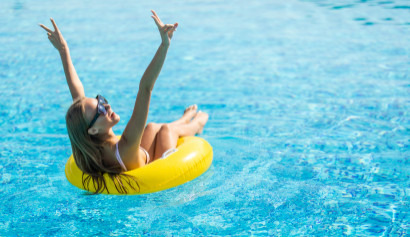 Frau sitzt mit Bikini in einem Schwimmreifen im Pool und zeigt das Peace Zeichen
