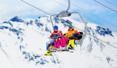 Familie mit bunten Skioutfits sitzen in einem Skilift Richtung Berg