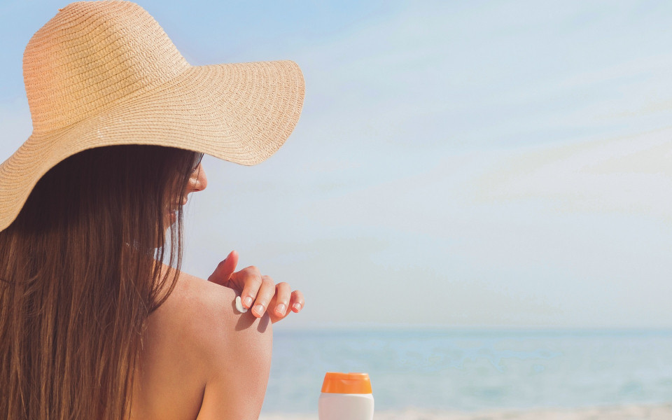 Frau mit Sonnencreme und Sonnenhut